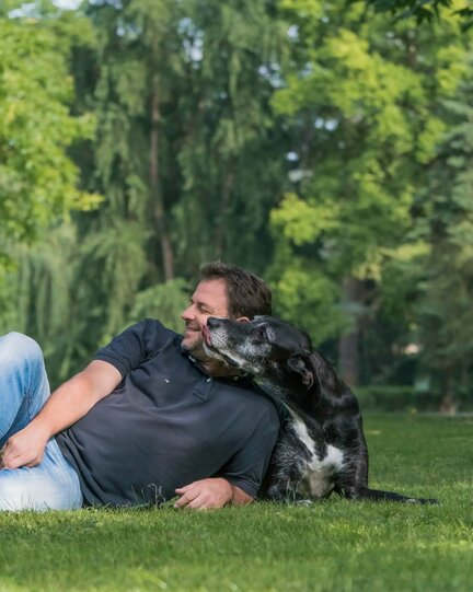 Liegender Martin Rütter, der von einem liegenden Hund geküsst wird