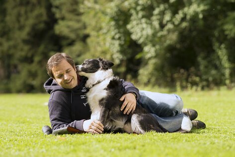 Martin Rütter liegt auf der Wiese und wird von seinem Hund Emma geküsst