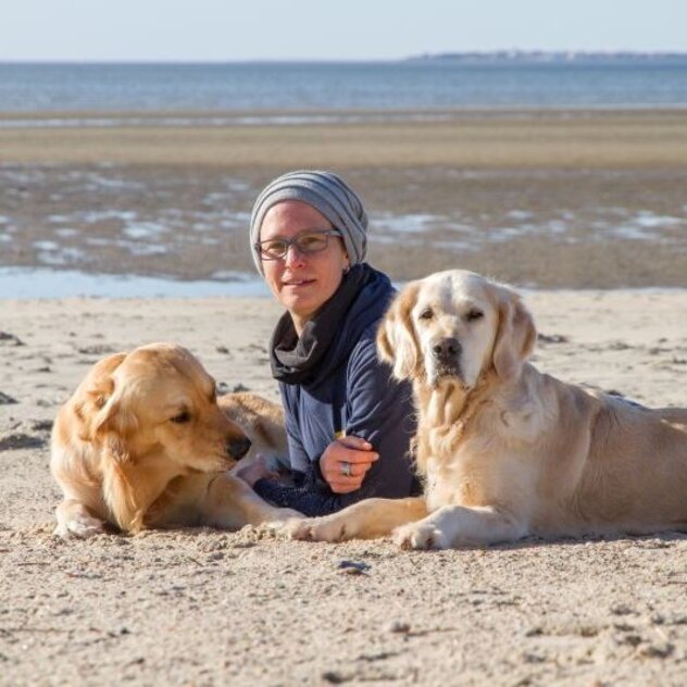 Hundetrainerin Christiane Reeg und ihre zwei Golden Retriever liegen im Sand