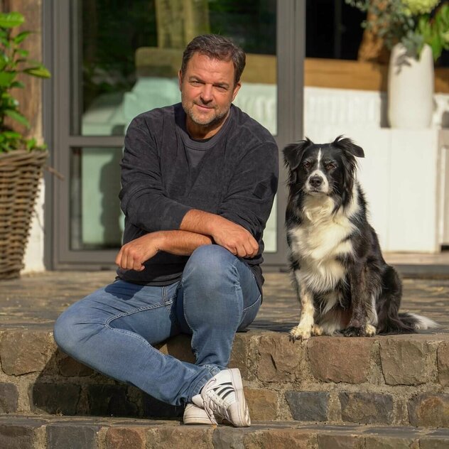 Martin Rütter sitzt mit seinem Hund Emma auf einer Treppenstufe