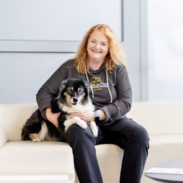Corinna Geis und ihre Australian Shepherd Hündin Grace sitzen auf einem weißen Sofa.