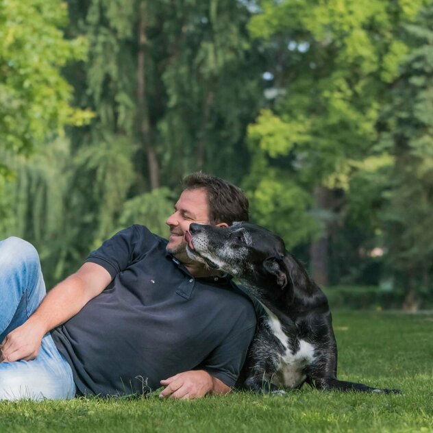 Liegender Martin Rütter, der von einem liegenden Hund geküsst wird