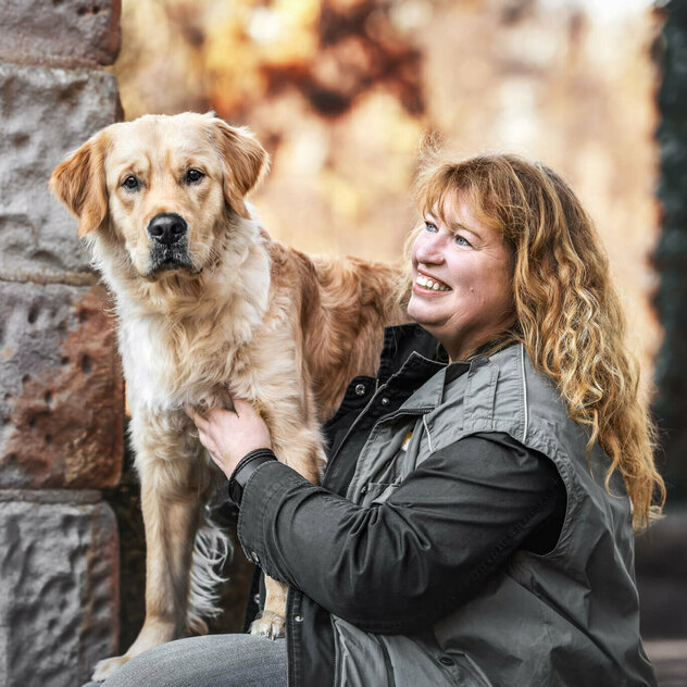 Frau mit blonden Haaren streichelt Hund, der erhöht steht