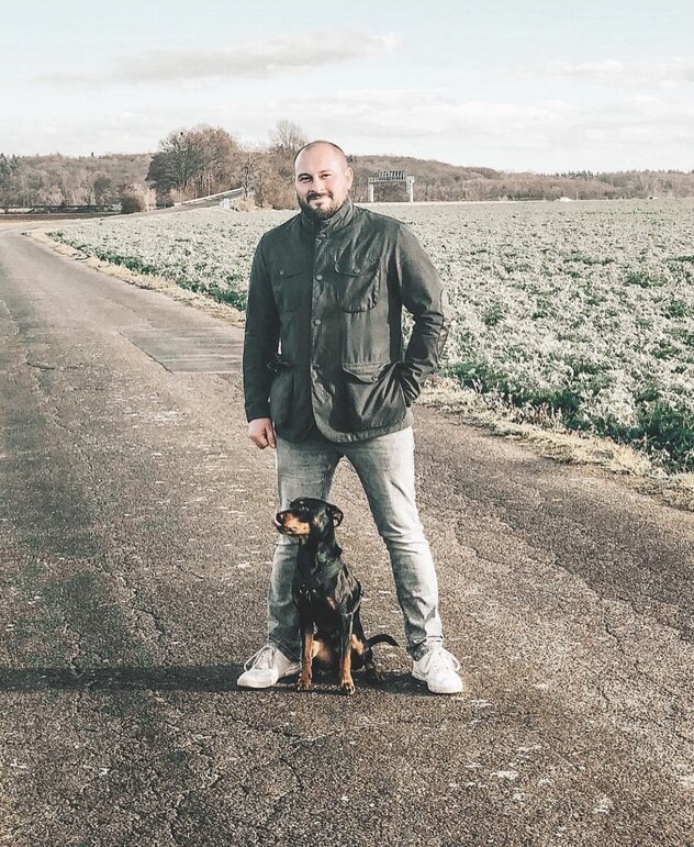 Mann im Feld mit Hund zwischen den Beinen