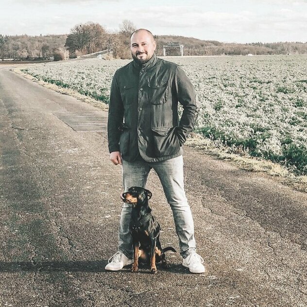 Mann im Feld mit Hund zwischen den Beinen