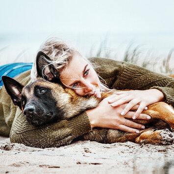 Frau liegt mit Malinois am Strand