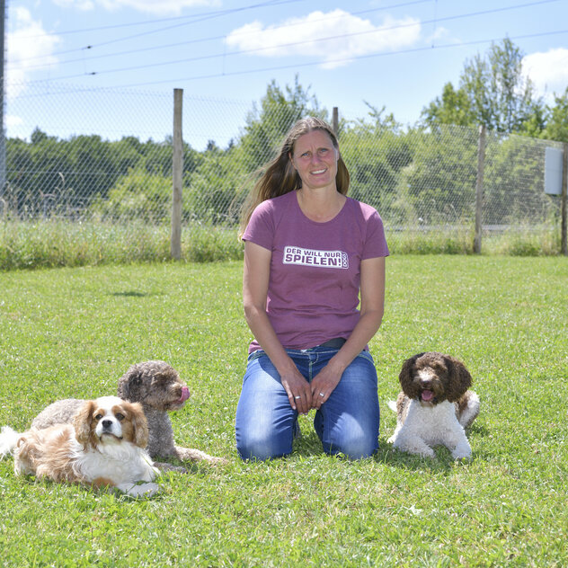 Claudia kniet auf Wiese mit drei Hunden