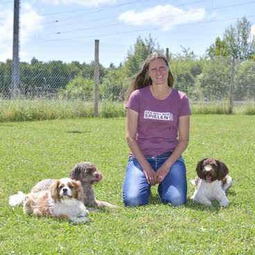 Claudia kniet auf Wiese mit drei Hunden