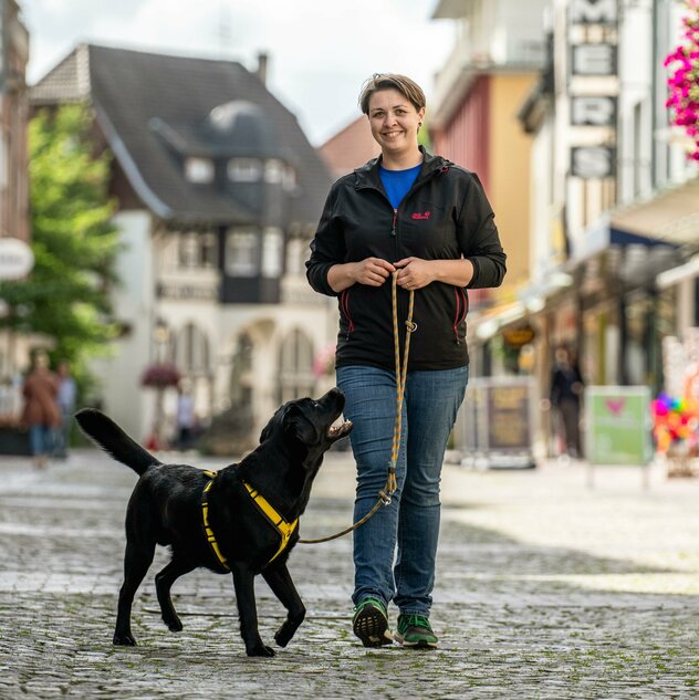 Alicia geht mit ihrem schwarzen Labrador Mando auf einer Kopfsteinpflasterstraße spazieren