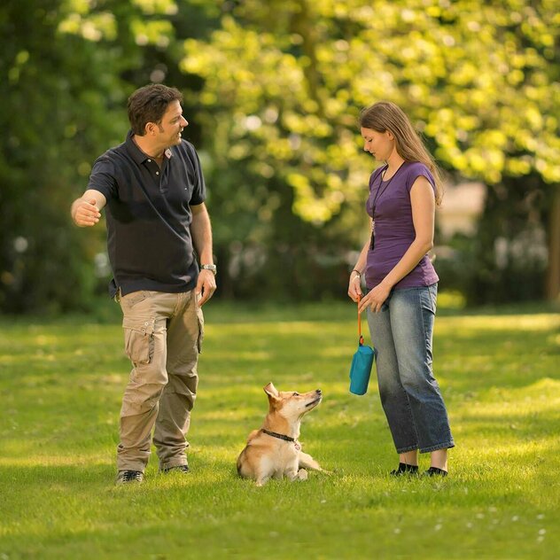 Martin Rütter im Gespräch mit Kunden, während Hund im Platz liegt und zu Frauchen und Futterbeutel schaut.