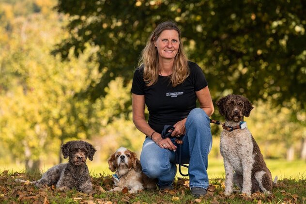 Claudia kniet mit 3 Hunden auf einer Wiese