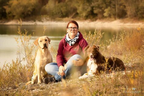 Steffi sitzt auf einer Wiese mit ihren beiden Hunden 