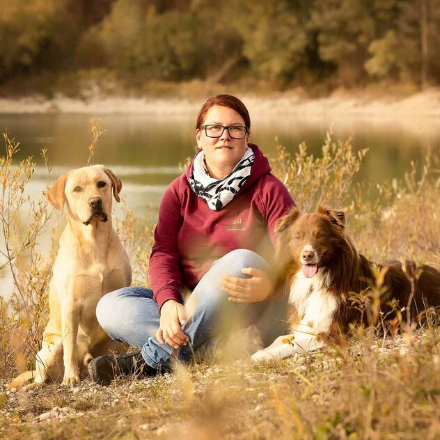 Steffi sitzt auf einer Wiese mit ihren beiden Hunden 